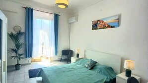 A hotel room with a bed, bedside tables, a chair, a desk, a potted plant, and a painting on the wall.