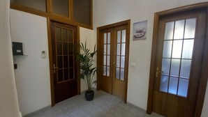 A hallway with two wooden doors, a potted plant, and a wall-mounted thermostat.