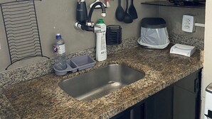 A kitchen with granite countertops, a stainless steel sink, a coffee maker, and utensils hanging on a rack. - Cozy Loft on Rua da Amizade - Itaipu (Itaipu Niterói)