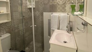 A bathroom with a glass-enclosed shower, a toilet, a sink, and a mirror. - Cozy Loft on Rua da Amizade - Itaipu (Itaipu Niterói)