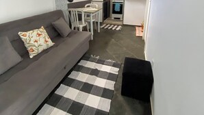 A compact living space with a sofa, a checkered rug, a kitchenette, and a dining area. - Cozy Loft on Rua da Amizade - Itaipu (Itaipu Niterói)