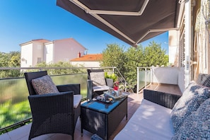 A balcony with wicker furniture, a table with a tray, and a view of a building and trees. - Apartment in Brodarica Near Beach & Krka Park (Sibenik)