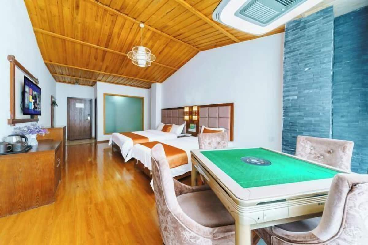 A hotel room with a wooden ceiling, a green pool table, two beds with orange bedding, and a stone accent wall.
