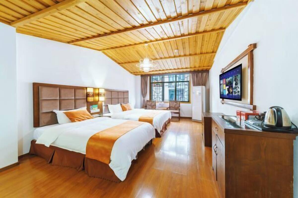 A hotel room with two beds, a wooden ceiling, a TV, and a desk with a kettle.