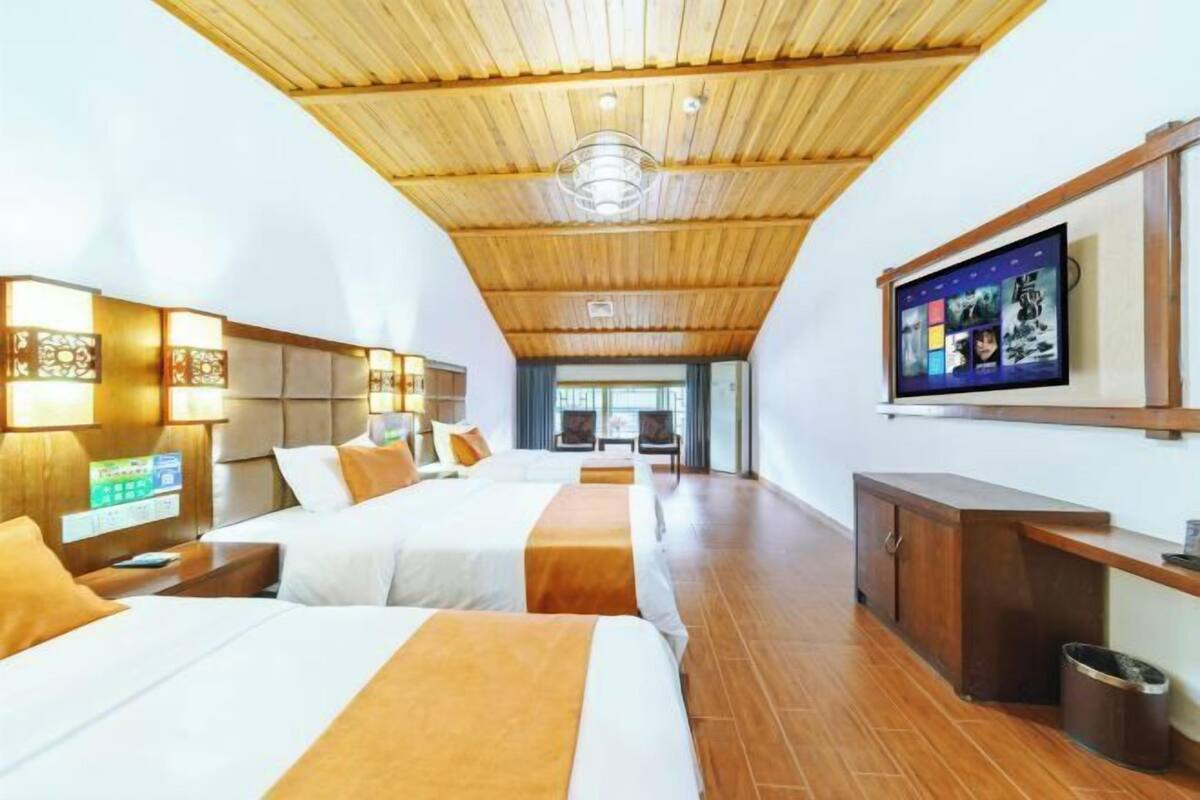 A hotel room with two beds, wooden ceiling, and a TV on the wall.