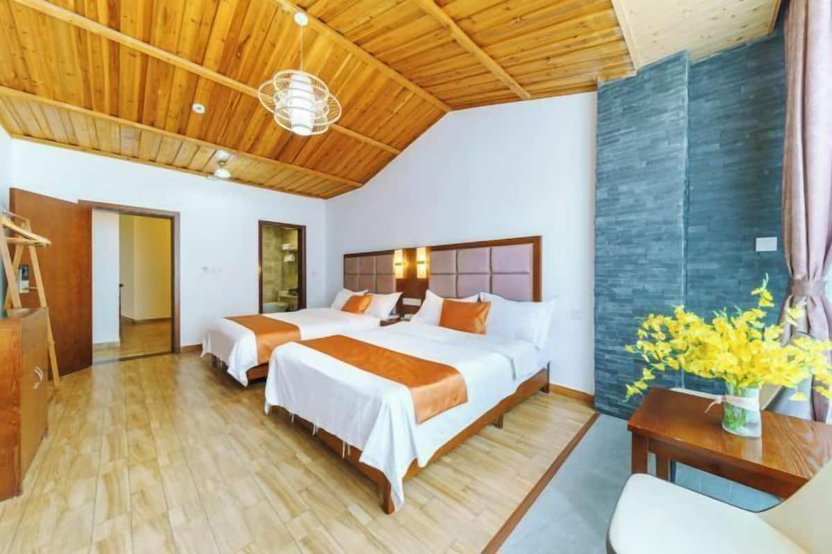 A hotel room with two beds, wooden ceiling, stone wall, and a small table with flowers.