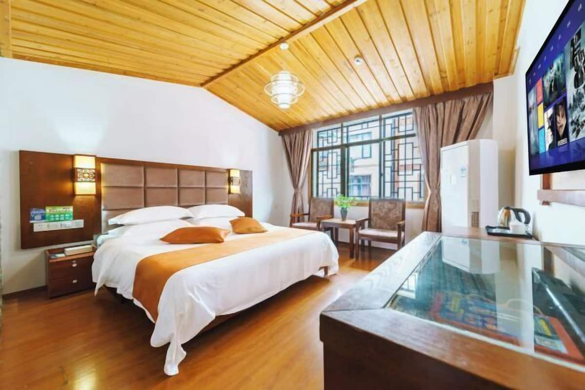 A hotel room with a wooden ceiling, a large bed with white bedding, a glass table, and a TV on the wall.