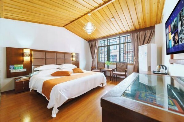 Une chambre d’hôtel avec un plafond en bois, un grand lit avec une literie blanche, une table en verre et un téléviseur fixé au mur.