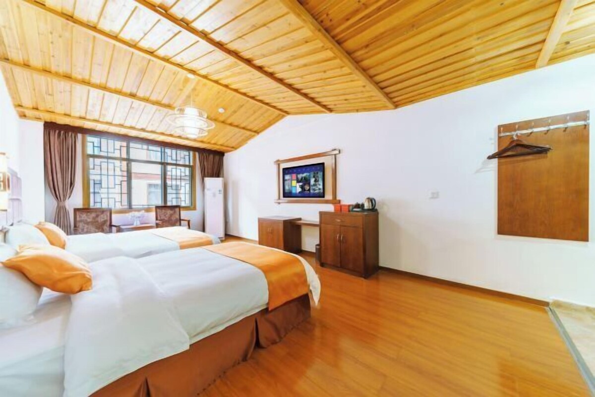 A hotel room with two beds, a desk, a TV, and a wooden ceiling.