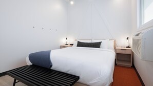 Una habitación de hotel moderna con una cama grande, mesitas de noche, un banco y una ventana.