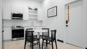 Una cocina moderna con armarios blancos, un horno de acero inoxidable, una mesa de comedor blanca con cuatro sillas y una puerta con un letrero.