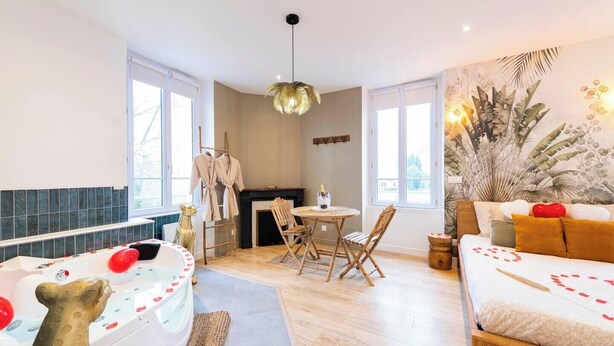 A room with a bathtub, a dining table, a sofa, and a fireplace. - Suite Savane with Jacuzzi 15min Disney (Nanteuil-lès-Meaux)