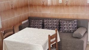 A dining area with a table covered in a white tablecloth, two wooden chairs, and a grey sofa with patterned cushions.