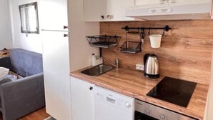 Une cuisine compacte avec des meubles blancs, un plan de travail en bois, un lave-vaisselle encastré, une cuisinière et une fenêtre au-dessus de l’évier.