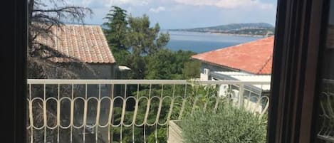A balcony with a metal railing, a potted plant, and a view of a coastal area with buildings and a body of water.