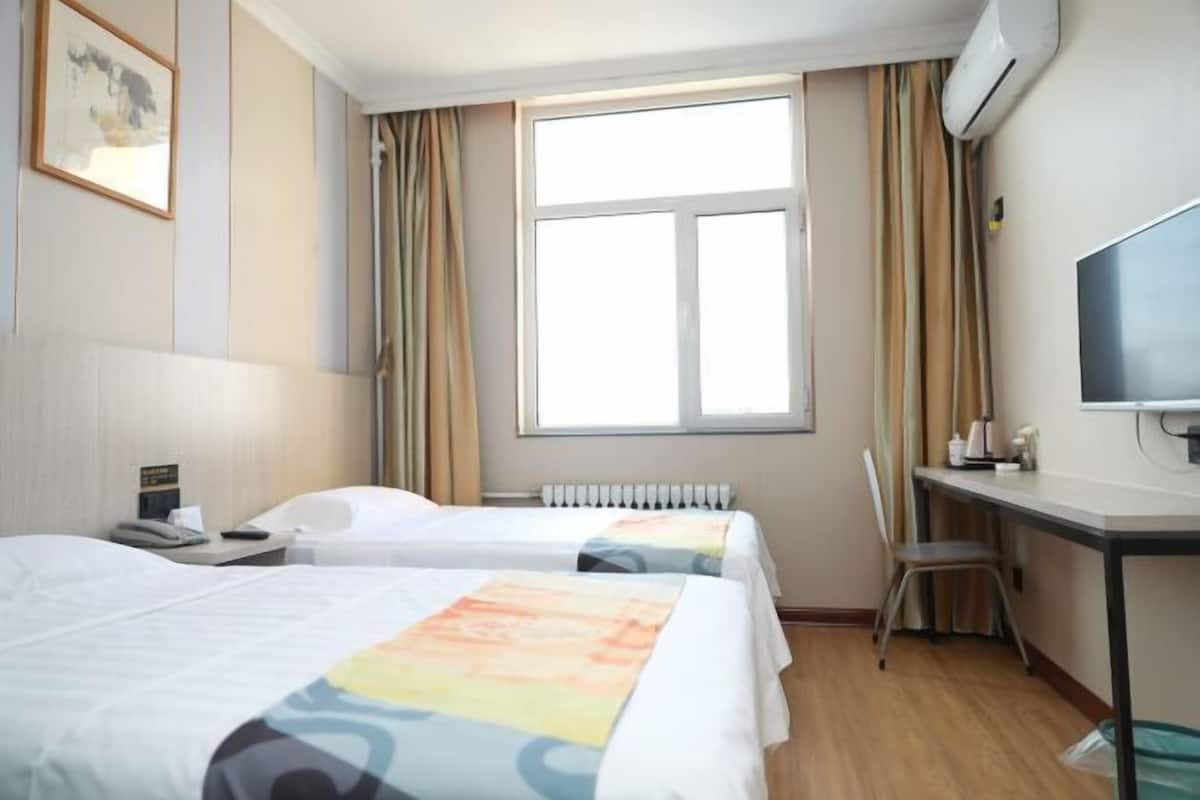 A hotel room with two beds, a desk, a chair, a TV, and a window with curtains.