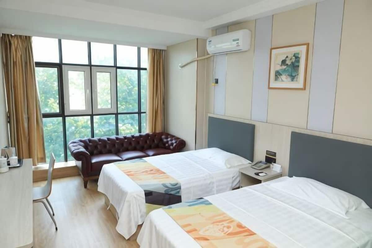 A hotel room with two beds, a leather sofa, a desk, and a window with curtains.