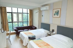 A hotel room with two beds, a leather sofa, a desk, and a window with curtains.
