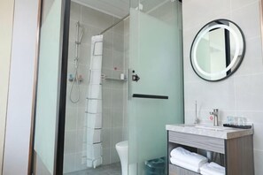 A bathroom with a glass shower enclosure, a toilet, a sink with a mirror, and a towel rack.