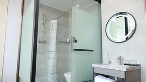 A modern bathroom with a glass shower enclosure, a toilet, a sink with a mirror, and a towel rack. - Shell Hotel (Zhaoyuan Wenquan Road) (Zhaoyuan)