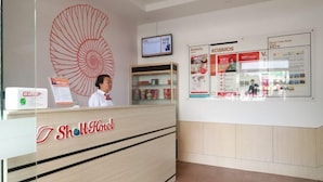 A hotel reception desk with a large shell decoration, a digital screen, and informational posters on the wall. - Shell Hotel (Zhaoyuan Wenquan Road) (Zhaoyuan)