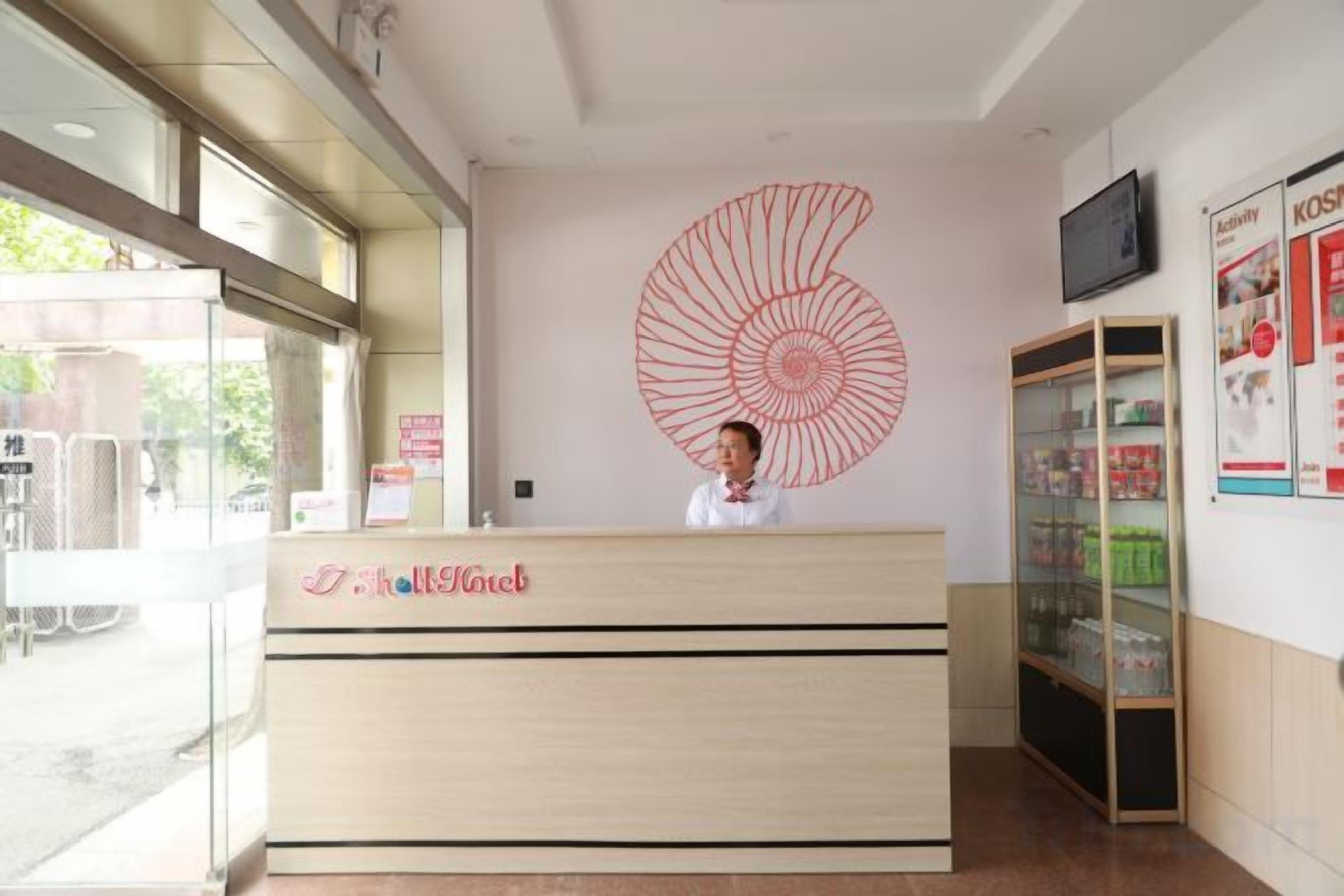 A hotel reception desk with a large spiral artwork on the wall, a reception area, and a glass display case with items.