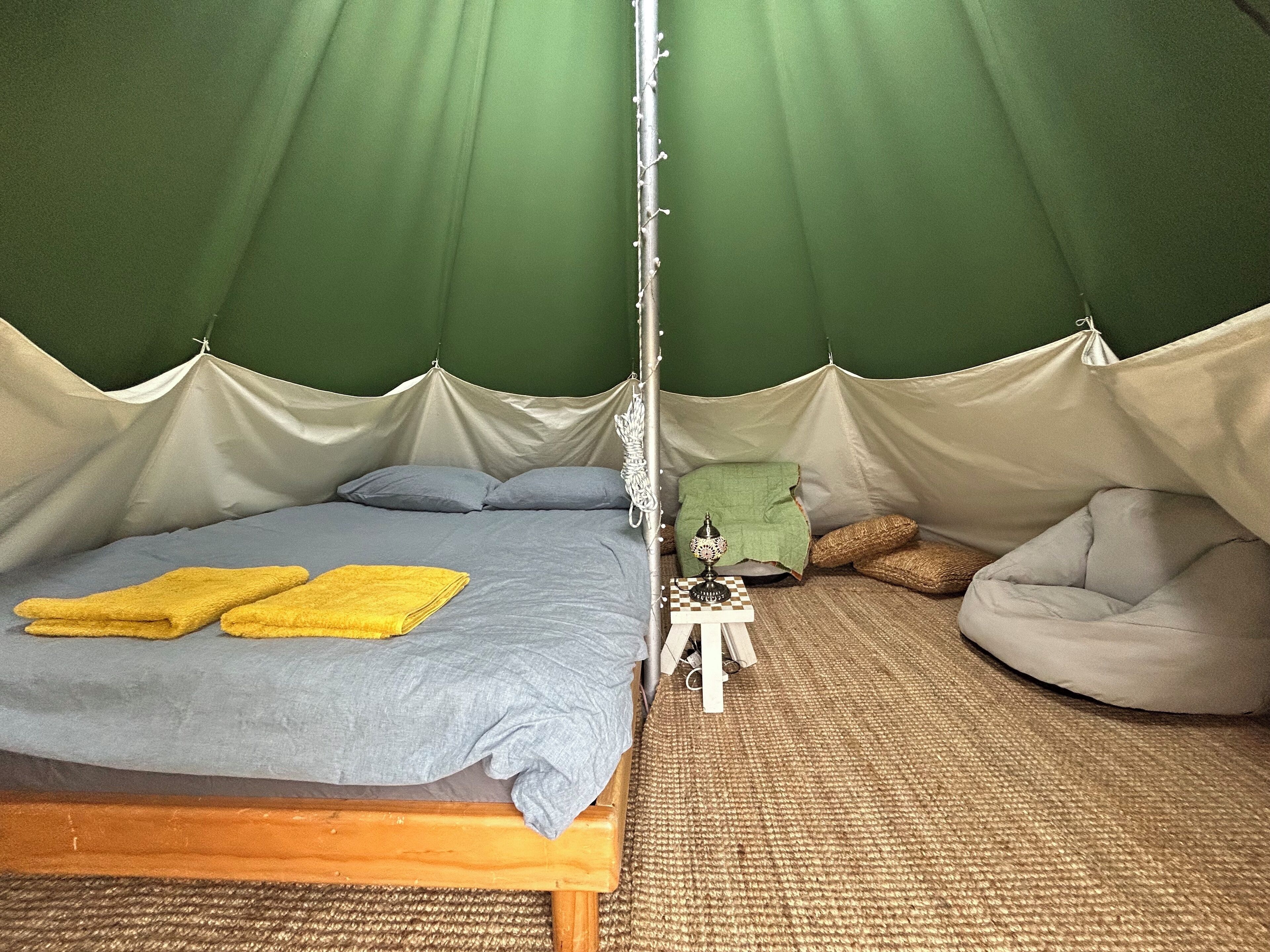 A tented room with a bed, a small table with a lamp, and a bean bag chair.