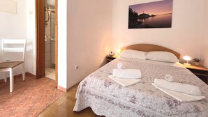 Un dormitorio con una cama, una silla, una mesita de noche y un cuadro de un atardecer.