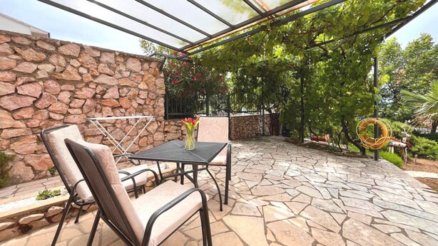 Un patio con suelo de piedra, sillas de metal, una mesa y un cerramiento de vidrio.