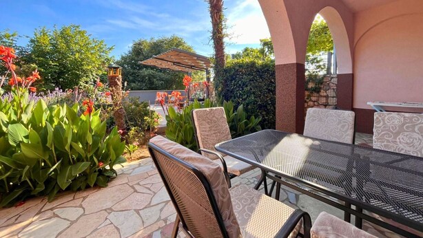 An outdoor patio with a table and chairs, surrounded by lush greenery and flowers.