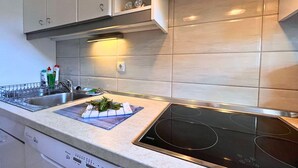 A modern kitchen with a built-in stove, a dish rack, and a countertop with a cutting board and vegetables.