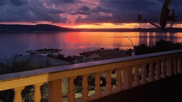 A sunset over a calm lake with a satellite dish and a balcony railing.