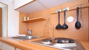 A kitchen with a double sink, a stove, and a wooden shelf above the sink.