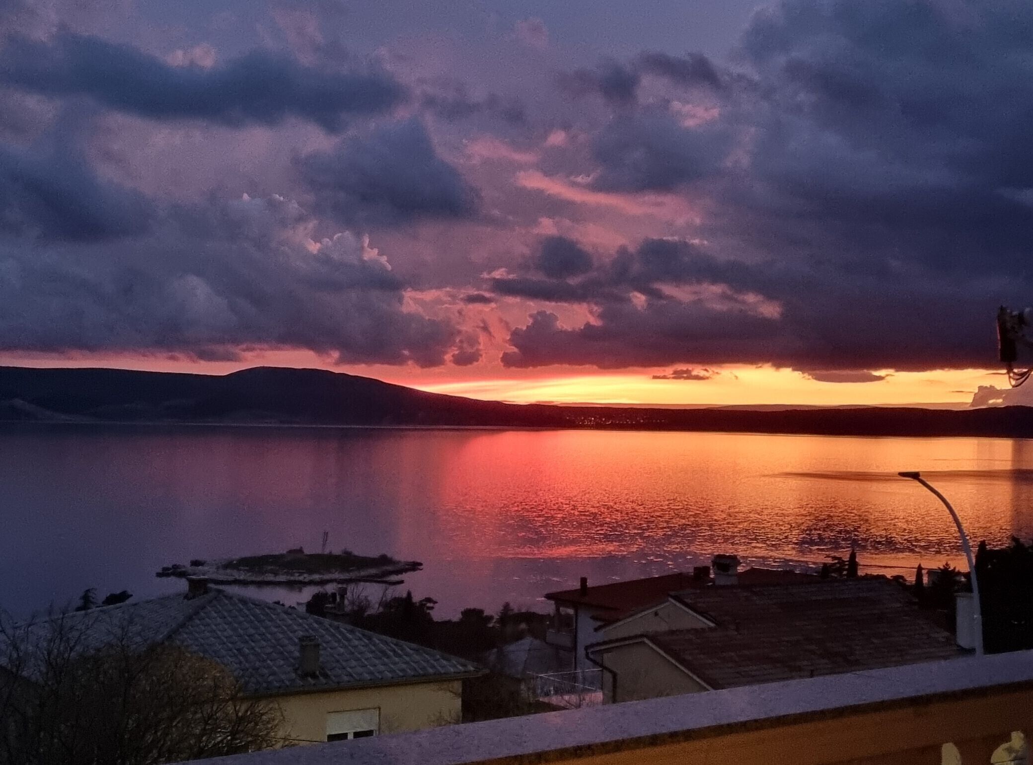 A sunset over a calm lake with a distant shoreline, surrounded by hills.