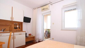 A bedroom with a bed, a desk with a chair, a TV, and a window.