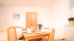 A cozy room with a wooden dining table set for breakfast, two single beds, a wooden wardrobe, and a small potted plant on a radiator.