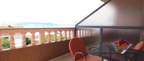 Un balcón con vista al mar, una mesa con sillas y un frutero.