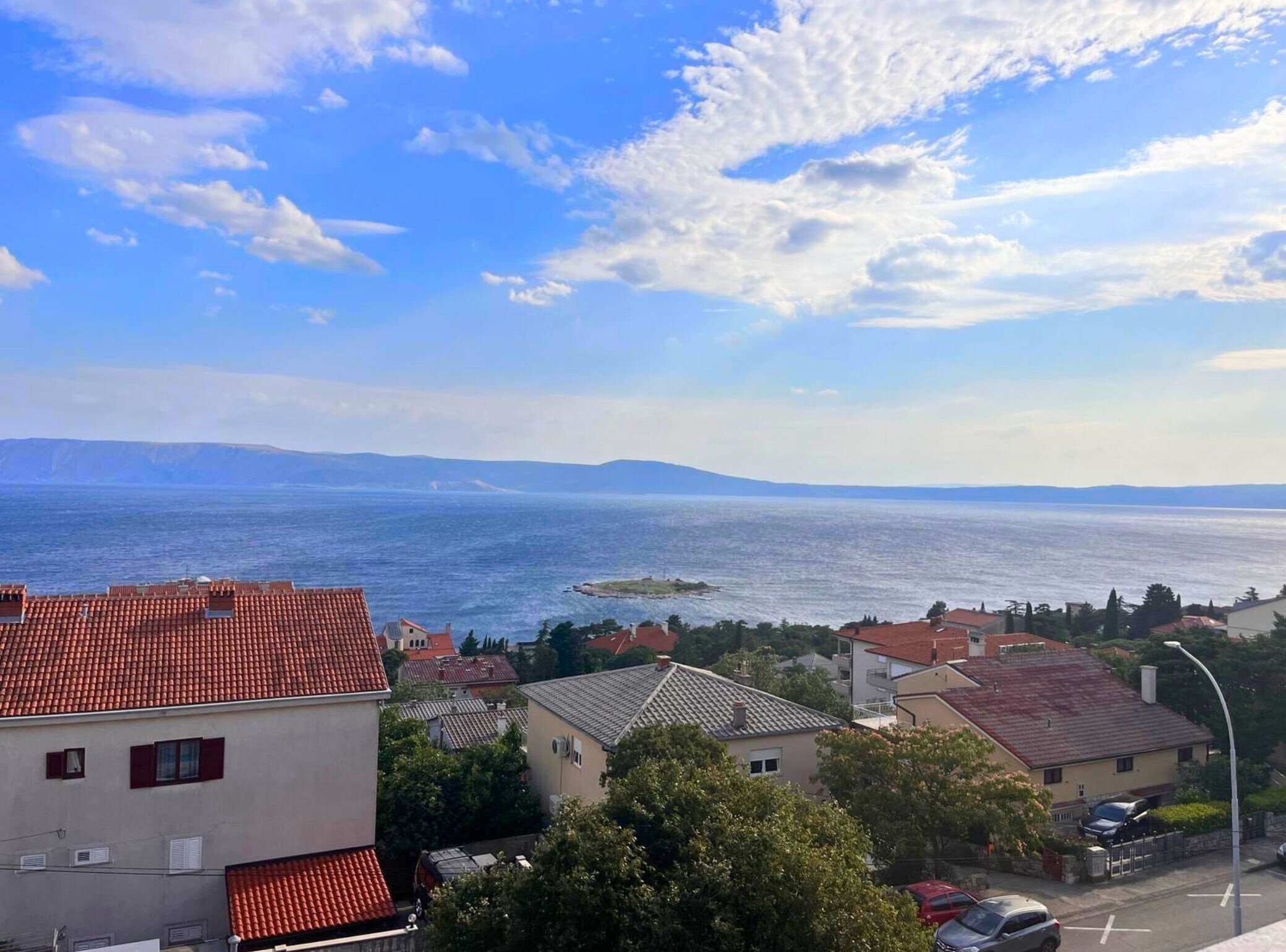 Un pueblo costero con tejados rojos, vista al mar y montañas a lo lejos.