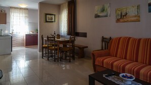 A living room with a striped sofa, a dining table with chairs, a kitchen area with a stove, and artwork on the walls.