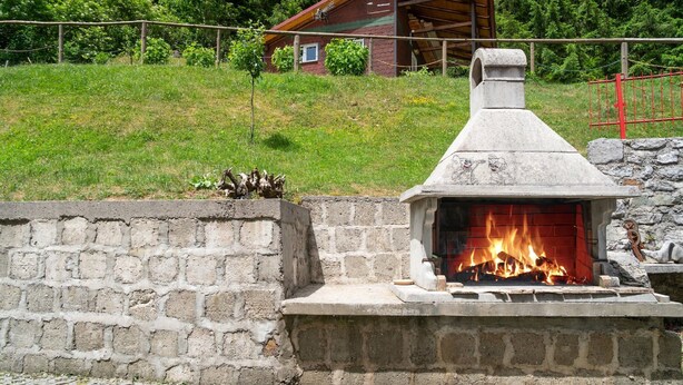 A stone-built outdoor fireplace with a chimney, surrounded by a stone wall and a grassy area.