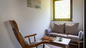 Um quarto aconchegante com uma cadeira de madeira, um sofá e um tabuleiro de xadrez sobre uma mesa.
