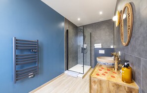 Ein modernes Badezimmer mit Duschkabine aus Glas, einem Handtuchhalter, einem Waschbecken mit dekorativer Schüssel und einem Holzwaschtisch mit Seifenspender.