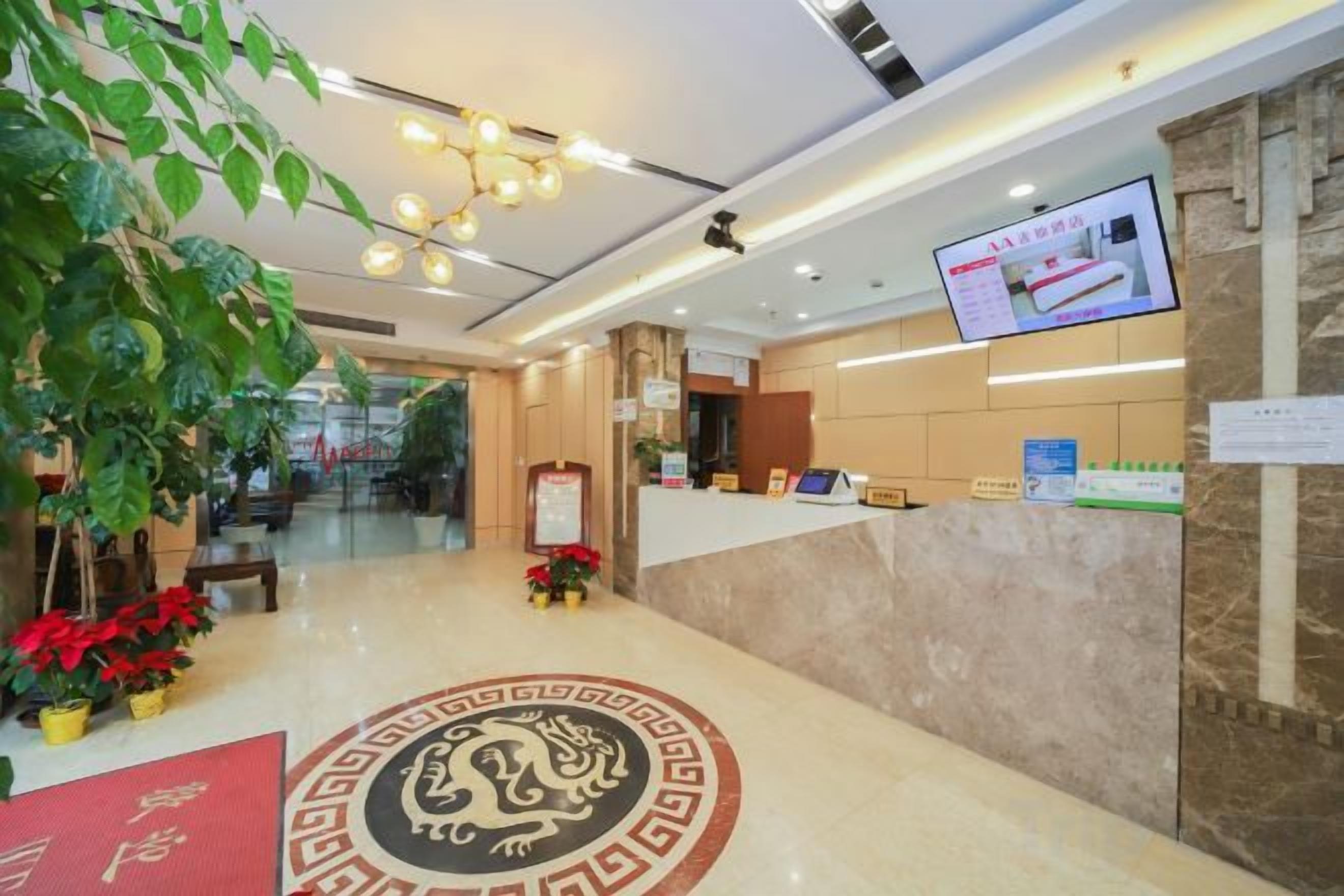 A hotel reception area with a reception desk, a digital screen, and a decorative circular emblem on the floor.