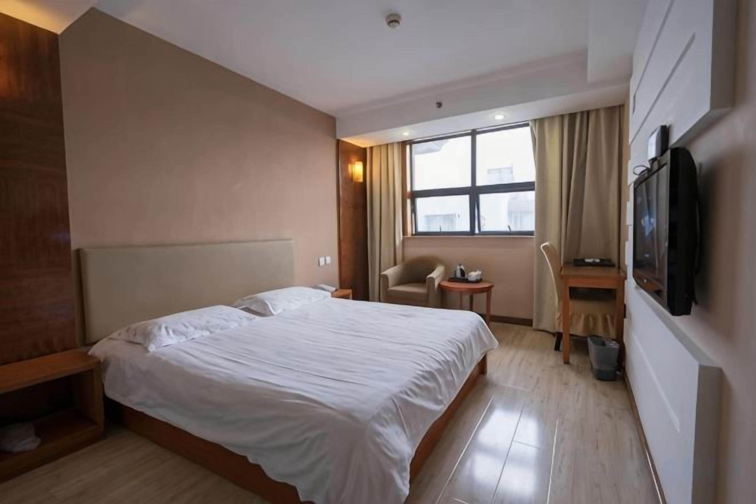 A hotel room with a bed, a desk, a chair, a television, and a window.