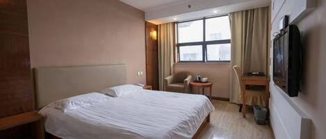 A hotel room with a bed, a desk, a chair, a television, and a window.