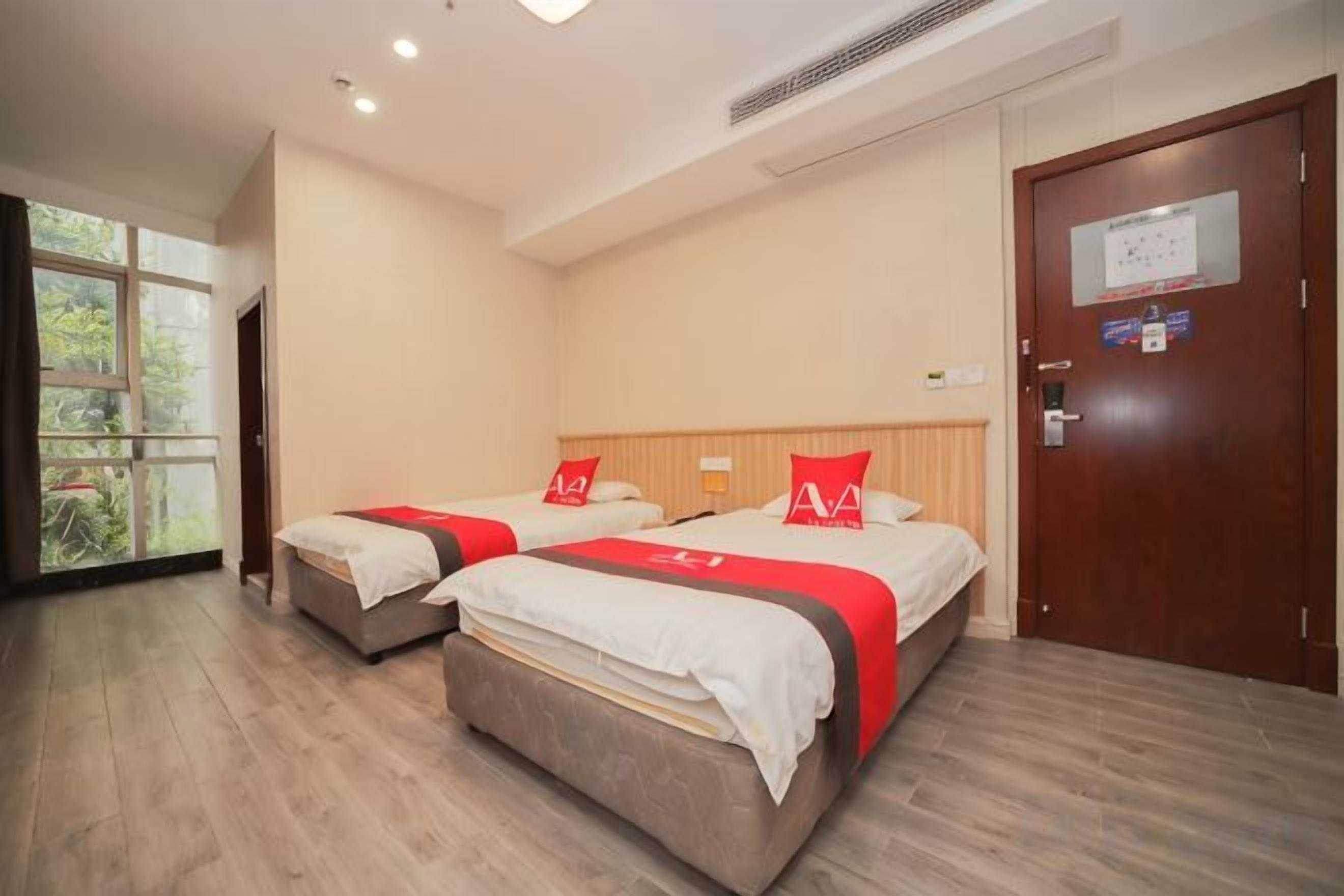 Een hotelkamer met twee bedden, een houten vloer, een raam met uitzicht en een deur met een bordje.