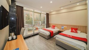 A hotel room with two beds, a desk with a chair, a TV, and a large window with a view of trees. - A&A Chain Hotel (Chuansha East Huaxia Road Subway Station) (Shanghai)
