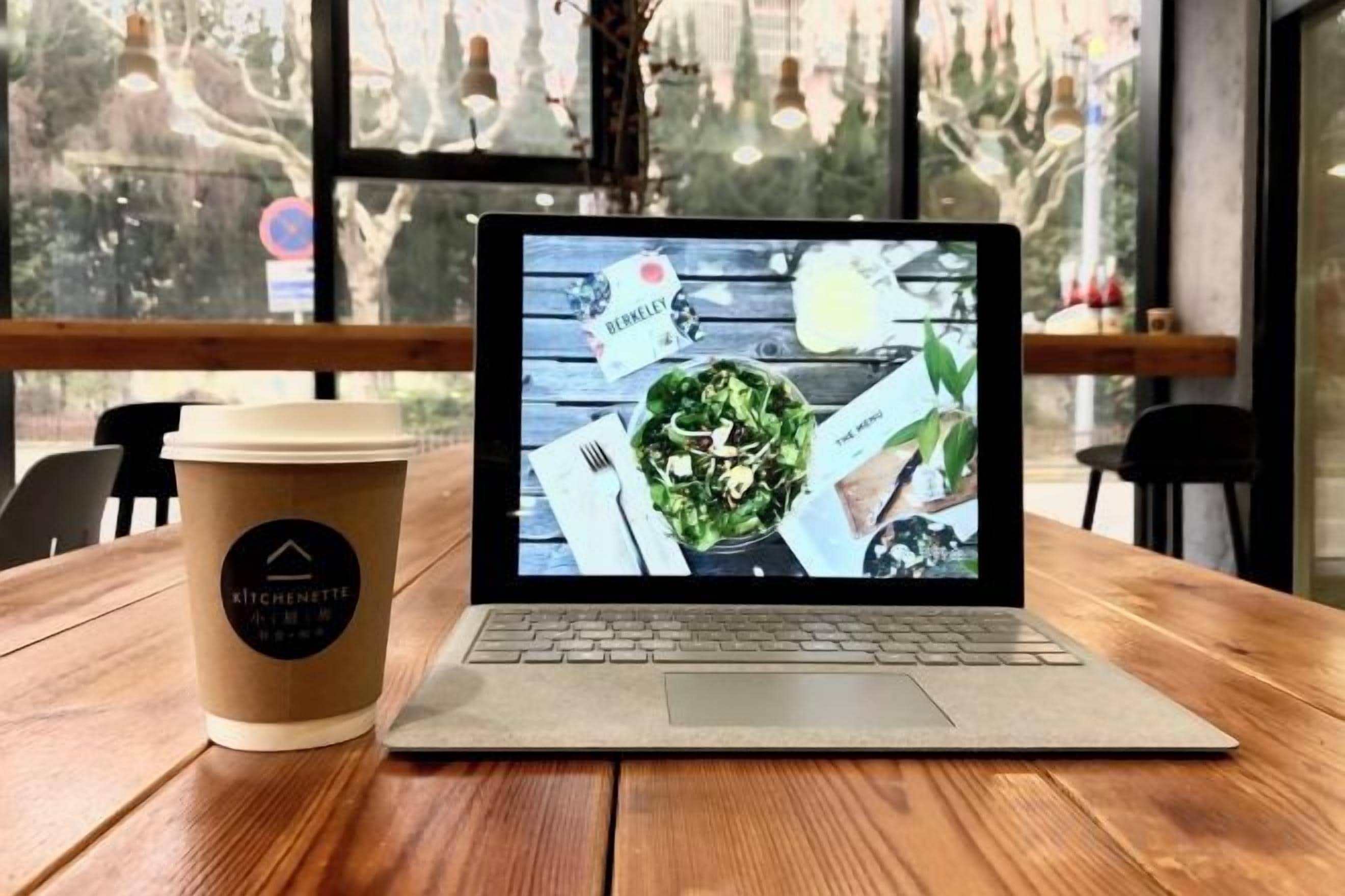A laptop on a wooden table with a coffee cup beside it.