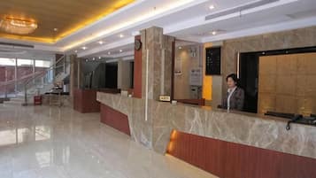 A hotel reception area with a marble counter, a staircase, and a large window.