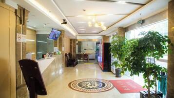 A hotel lobby with a reception desk, seating area, and a large potted plant.